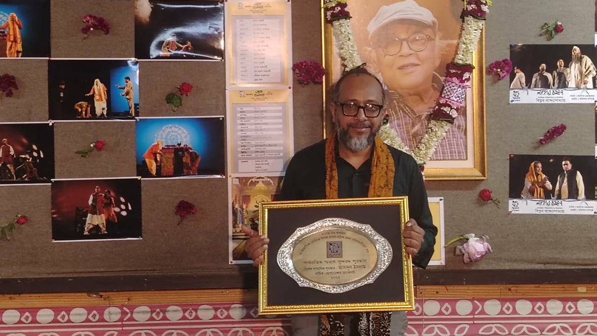 মনোজ মিত্রের ছবির সামনে তারই প্রবর্তন করা প্রতিযোগিতার পুরস্কার হাতে আসাদুল ইসলাম। ছবি: আসাদুল ইসলামের সৌজন্যে