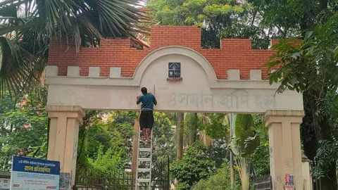 ফটকে থাকা ‘শহীদ ওসমান হাদি হল’ লেখা মোছা হচ্ছে। ছবি: সংগৃহীত