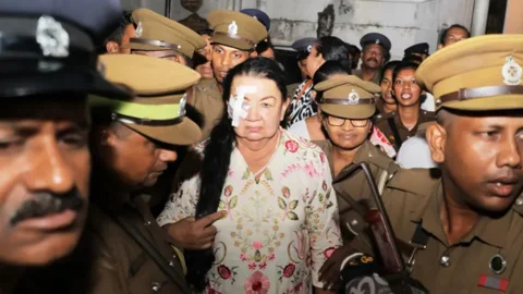 কলম্বোয় ম্যাজিস্ট্রেট আদালতের বাইরে কারাগারের গাড়িতে ওঠানোর আগে শিরান্থি রাজাপাকশেকে নিয়ে যাচ্ছেন কারা কর্মকর্তারা। ৭ অক্টোবর ২০২৬। ছবি: সংগৃহীত